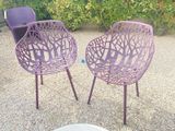two purple chairs sitting next to each other in a gravel area