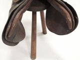 a brown saddle on a wooden stand on a white surface