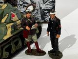 two figurines of men standing next to a toy tank