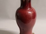 un vase rouge avec un couvercle doré posé sur une surface blanche