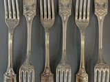 six forks and a spoon are arranged in a row on a table