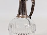 a silver and glass vase with a handle on a white surface