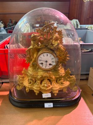 a gold clock under a glass clochet on a table
