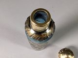 a silver and blue vase with a gold lid next to a small gold object