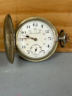 une vieille montre de poche posée sur une table, à côté d'un morceau de bois