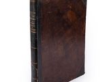 an old book with a brown cover sitting on top of a white surface
