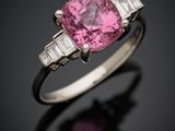 une bague sertie d'un saphir rose et de diamants, posée sur un fond noir