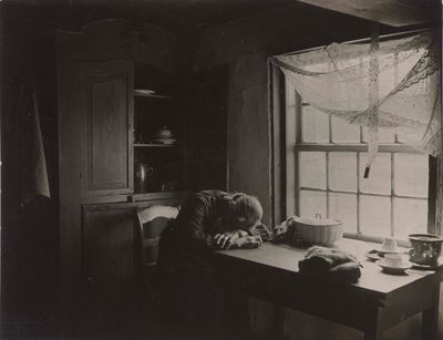 black and white photograph of a cat sitting at a table in front of a window