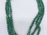 un gros plan d'un collier de perles vertes posé sur une surface blanche