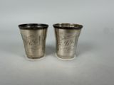 two silver cups with etched designs on them on a white surface