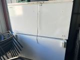 a white refrigerator sitting in a garage next to a stack of chairs