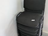 a stack of black chairs next to a table with a laptop on it