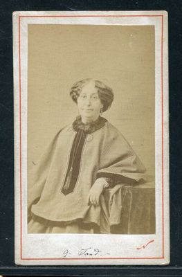 une vieille photo d'une femme assise sur une chaise, vêtue d'un châle