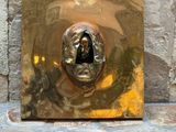 une plaque en or sur laquelle est représenté un visage, posée sur un sol en pierre