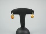 une paire de boucles d'oreilles en forme de coquillage dorées, posées sur un support noir