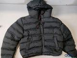 La veste est noire et comporte une capuche fixée à l'arrière de la veste.