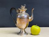 a silver tea pot next to an apple on a table