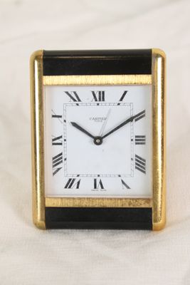 une image représentant une horloge noire et dorée posée sur un drap blanc
