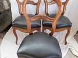 four chairs with black leather upholstered seats and a wooden frame