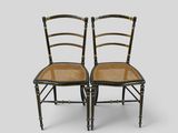 a pair of black and gold painted chairs with cane seats