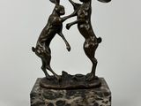 une statue en bronze représentant deux lapins qui se battent, posée sur un socle en marbre