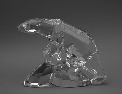 un ours en cristal assis sur un rocher, sur un fond gris