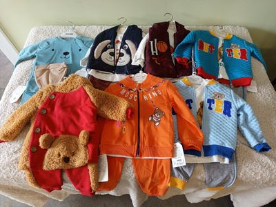 a lot of baby clothes on a bed with a teddy bear