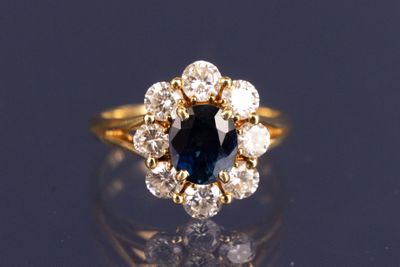 un gros plan d'une bague sertie d'un saphir bleu et de diamants, posée sur une surface réfléchissante