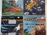 Quatre albums de bandes dessinées sont alignés sur une surface blanche