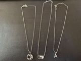 three silver necklaces with initial charms on them sitting on a table