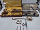 des couverts rangés dans un coffret posé sur une table, à côté d'autres couverts
