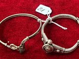 une paire de bracelets en argent posée sur un tissu rouge, avec une étiquette de prix