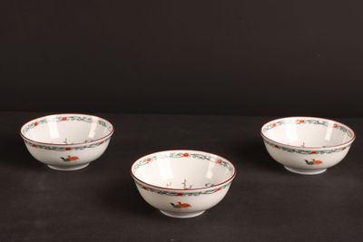 three white bowls with red and green designs on them on a black surface