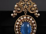 un gros plan d'une broche ornée de perles et d'une pierre bleue