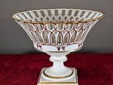 a white and gold bowl on a stand on a red surface