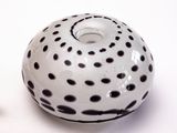 un vase blanc parsemé de taches noires, à côté d'un petit objet blanc
