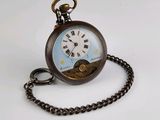 une montre de poche attachée à une chaîne, posée sur une surface blanche