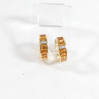 une paire de boucles d'oreilles en or jaune et diamants posées sur une surface transparente