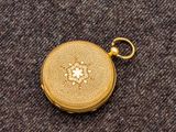une image représentant une montre de poche en or posée sur un tissu marron
