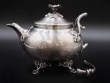 une théière ancienne en argent posée sur un socle, sur fond noir