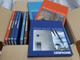 several books in a cardboard box on a bed with a white sheet