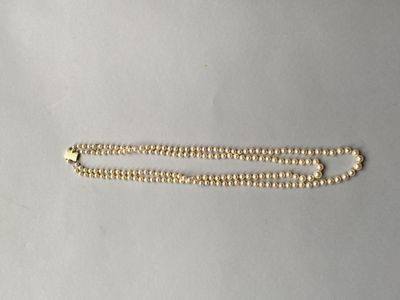 un gros plan d'un collier de perles dorées posé sur une surface blanche