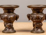 une paire de vases anciens en bronze posés sur une table en bois, sur fond gris