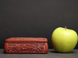 a green apple next to a red box on a table