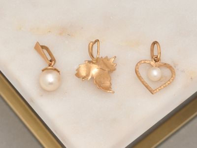 three gold - plated charms and a pearl heart on a marble surface