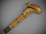 a close up of a wooden walking stick with a gold and black design