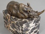 statue of a rhino lying on a marble block with a gray background