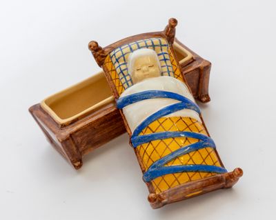 une poupée miniature représentant un homme allongé dans un lit, avec un bandage autour du cou