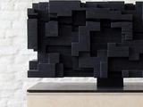 a black sculpture on a wooden block on a table