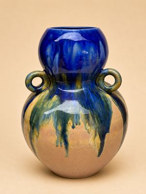 un vase bleu et vert posé sur une surface beige